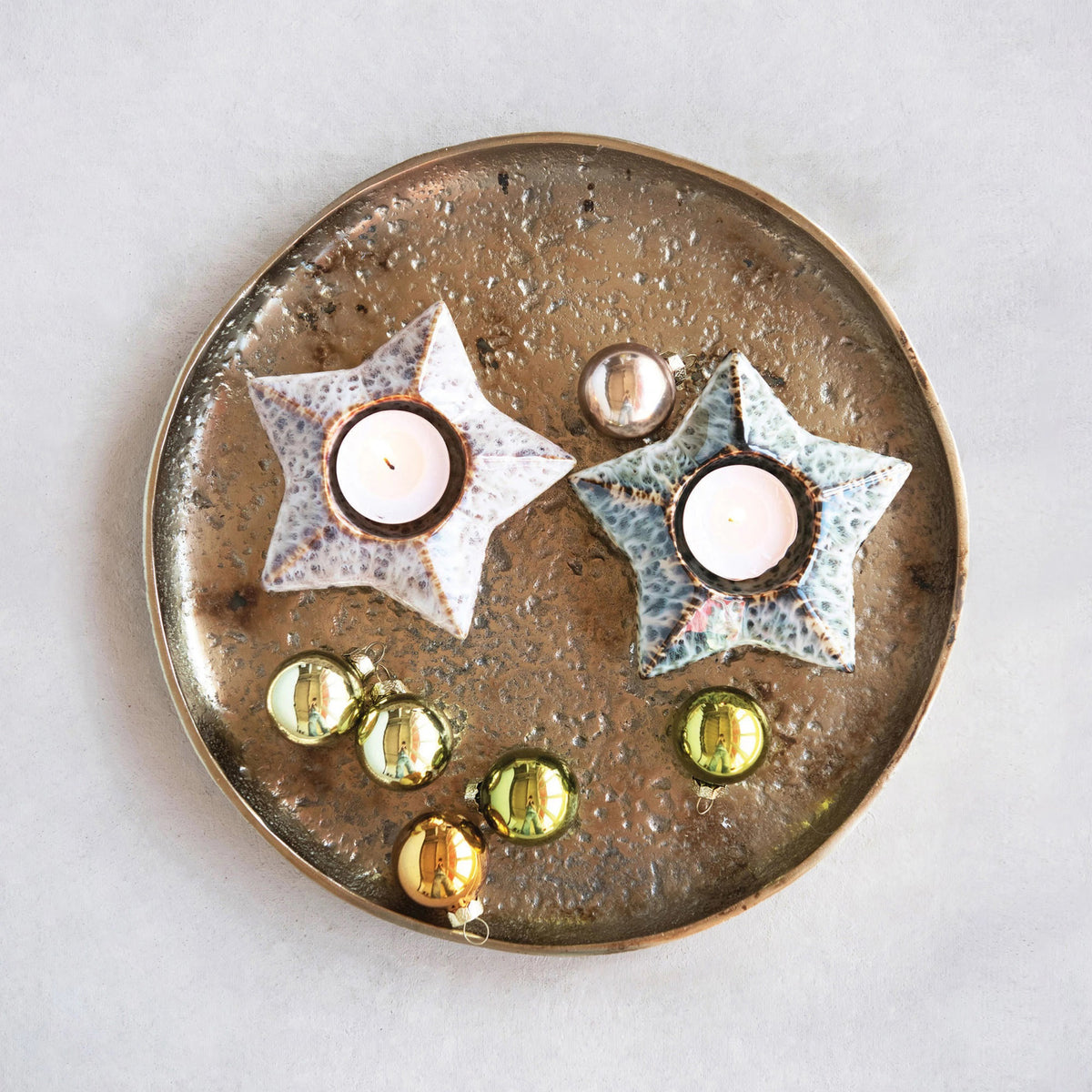 A minimalist winter scene featuring the CREATIVE COOP STONEWARE STAR TEALIGHT HOLDER, stoneware and ceramic pine trees, wooden log vases with pine branches, a fluffy white owl figurine, all arranged on a light wooden table against a plain white wall.
