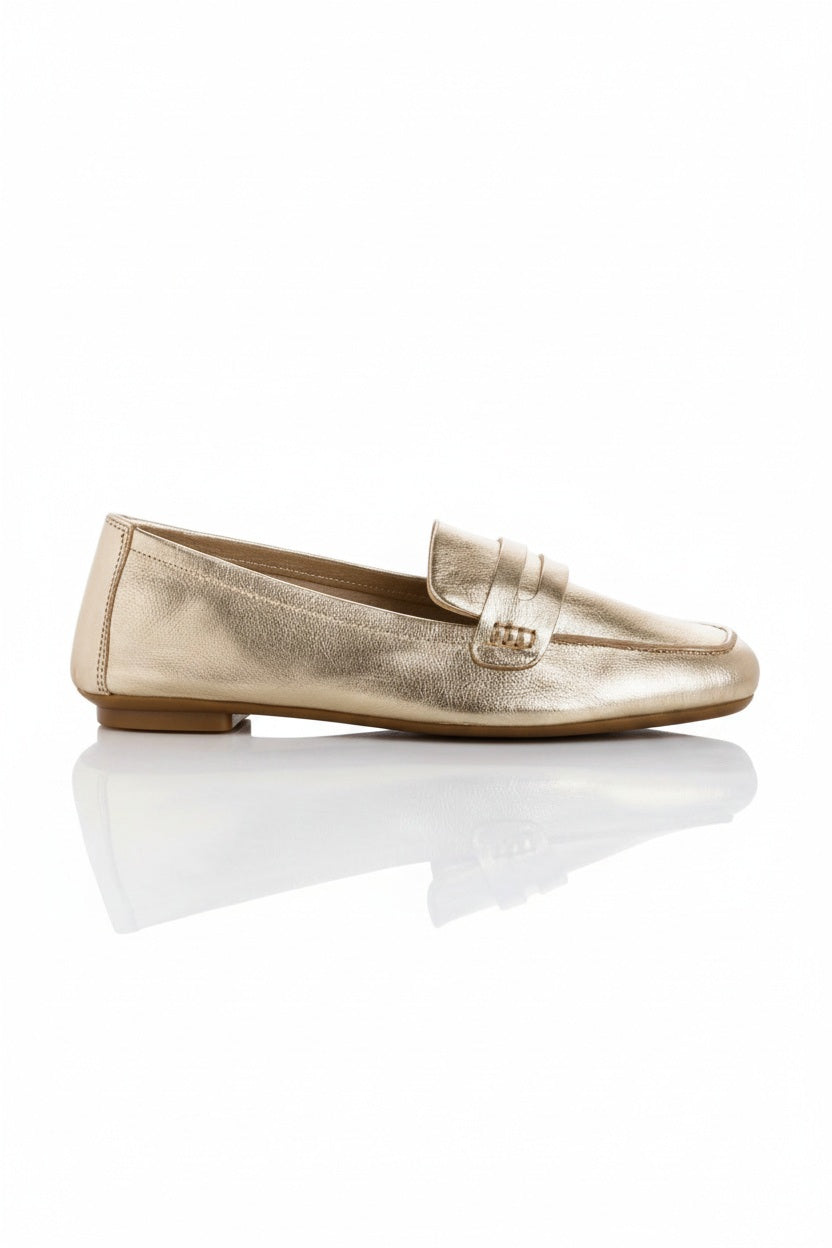 The REQINS - HEMA Metallic Loafer in Platinum features shimmering leather, a low heel, and a decorative front strap, showcased on a plain white background.