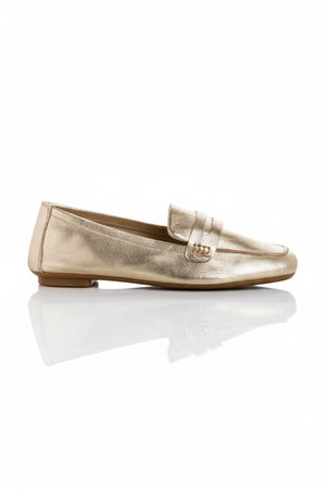 The REQINS - HEMA Metallic Loafer in Platinum features shimmering leather, a low heel, and a decorative front strap, showcased on a plain white background.