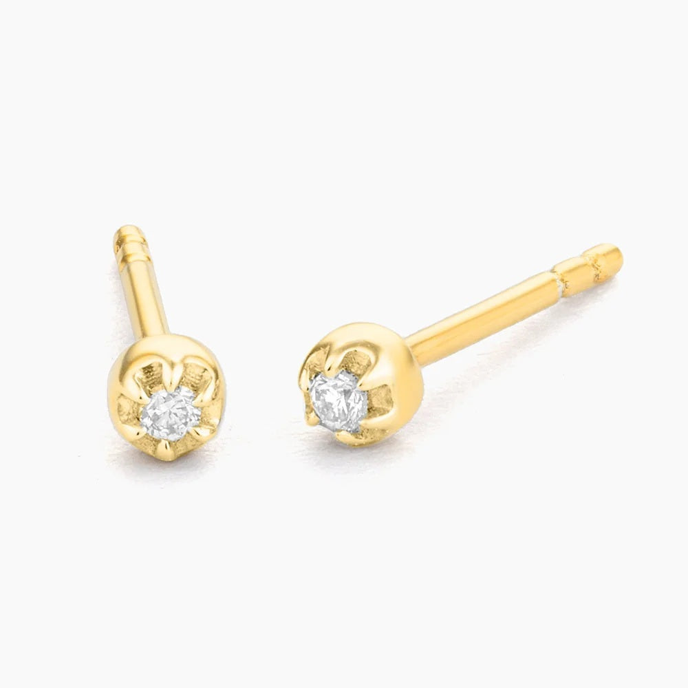 Close-up of a woman’s ear wearing the ELLA STEIN - ALA STUD EARRINGS by ELLA STEIN, featuring a small, round natural diamond. Her brown hair is pulled back, with a softly blurred background hinting at an outdoor setting.