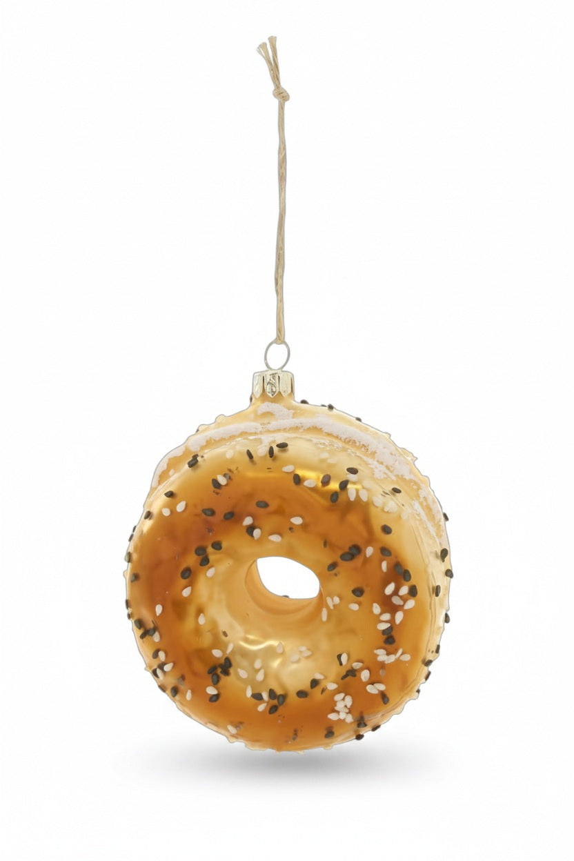 Cody Foster Everything Bagel Ornament made of glass and topped with sesame and poppy seeds, hanging from a string.