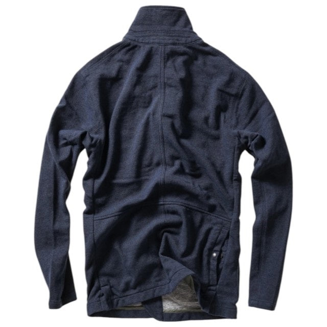 A person wearing the RELWEN - PIQUE TRAP BLAZER IN NAVY HEATHER over a checked shirt and green cargo pants stands with hands in pockets against a plain background, showcasing the blazer’s relaxed fit.