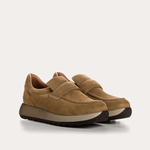 The REQINS - CARABEL Suede Sneaker in Havana is a tan goat suede casual-chic slip-on trainer featuring a rounded toe, wide instep strap, cushioned collar, and a thick dark rubber sole with a textured tread; shown in profile on a white background.