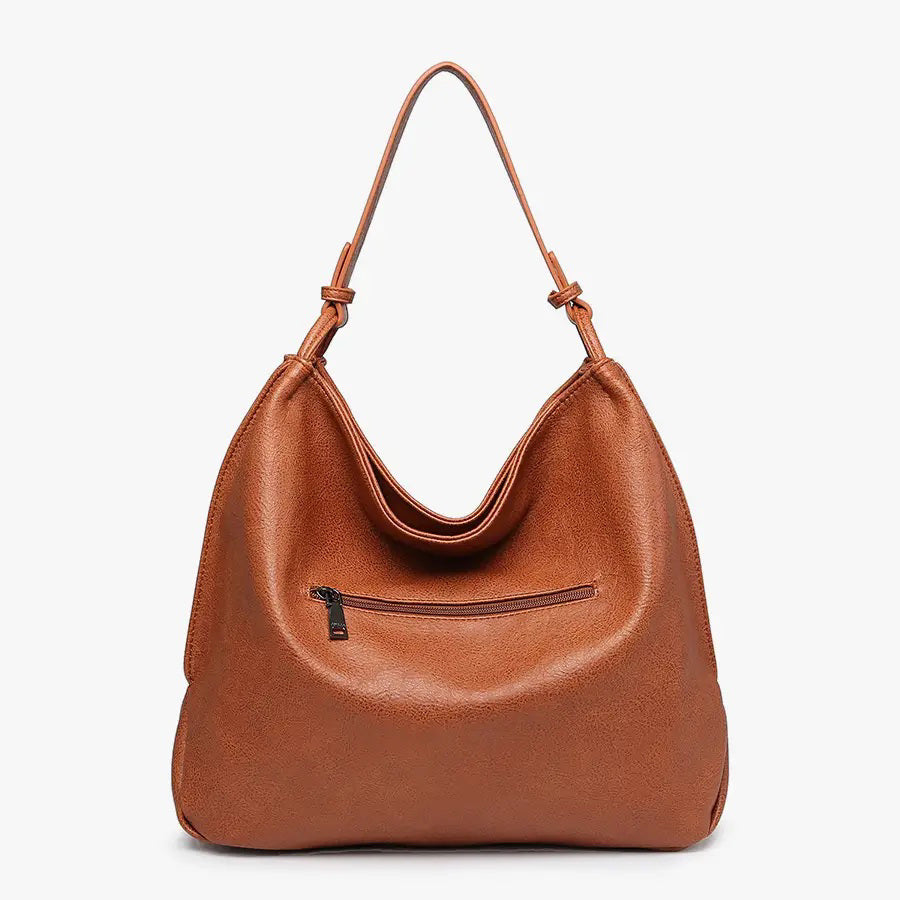 The JEN &amp; CO RUSTIC TOTE is crafted from brown vegan leather and features a relaxed, slouchy shape. Its simple and elegant design includes a single strap attached at both sides, along with an inner compartment for added functionality, all set against a plain light background.