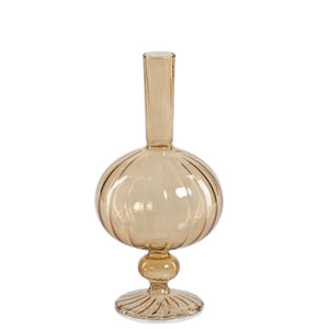 Five amber glass vases of varying heights and shapes, including the striking ZODAX VENETIAN SPIRAL VASE IN AMBER ONION SHAPE (7.5”), are arranged together on a textured surface. Some contain delicate, decorative branches with small beads, set against a softly lit, neutral-toned background.