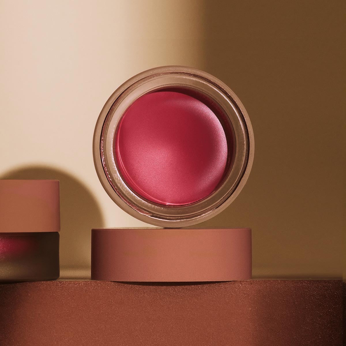 An open jar of MINORI - CREAM BLUSH in the shade Sweet Pea, featuring a pink lid and revealing a smooth, rosy pink cream-to-powder formula inside the clear container for a natural-looking blush finish.