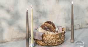 Two PIFFANY UYUNI Ivory Slim Taper Candles (1x12.6) with small yellow flames stand upright side by side against a plain white background, exuding timeless elegance.