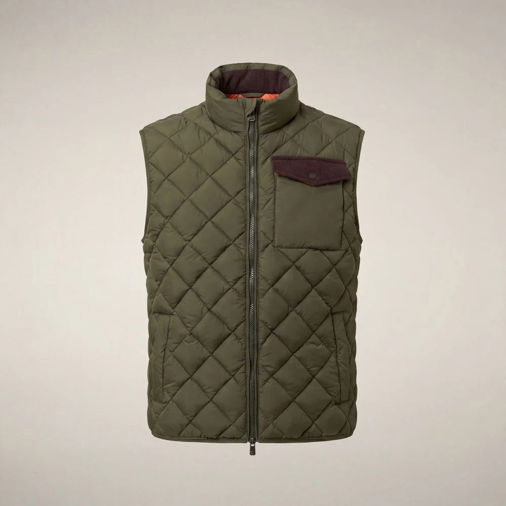 A person stands facing forward, wearing the SAVE THE DUCK - FABRICE Puffer Vest in Snake Green with Plumtech® padding over a beige sweater, paired with white pants and tan shoes, against a plain light background.
