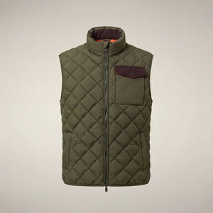 A person stands facing forward, wearing the SAVE THE DUCK - FABRICE Puffer Vest in Snake Green with Plumtech® padding over a beige sweater, paired with white pants and tan shoes, against a plain light background.