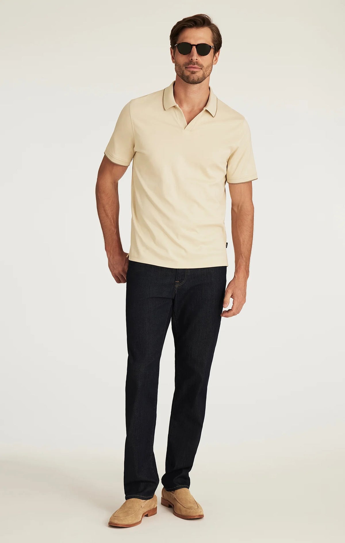 A person wearing 34 HERITAGE - CHARISMA RELAXED STRAIGHT JEANS IN RINSE VINTAGE, a dark blue, vintage-inspired denim by 34 HERITAGE, paired with a beige shirt and shown from the back. The jeans feature brown stitching and a brown leather patch on the waistband.