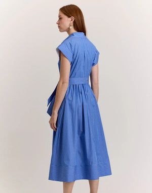 A woman with long brown hair models the HINSON WU Annabelle Short Sleeve Dress in Lake Blue Pencil Stripe, featuring a collared, button-down 100% cotton design with a matching waist tie. She stands against a plain light background.