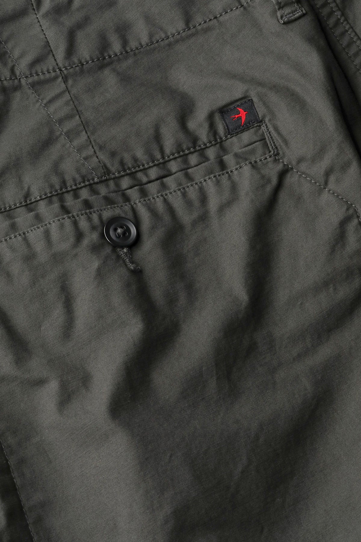 The RELWEN Flyweight Flex Chino in Charcoal, shown from the back with two buttoned pockets and subtle wrinkling, features a slim, straight-leg fit and lightweight stretch fabric for comfort. Pants are displayed flat on a white background.