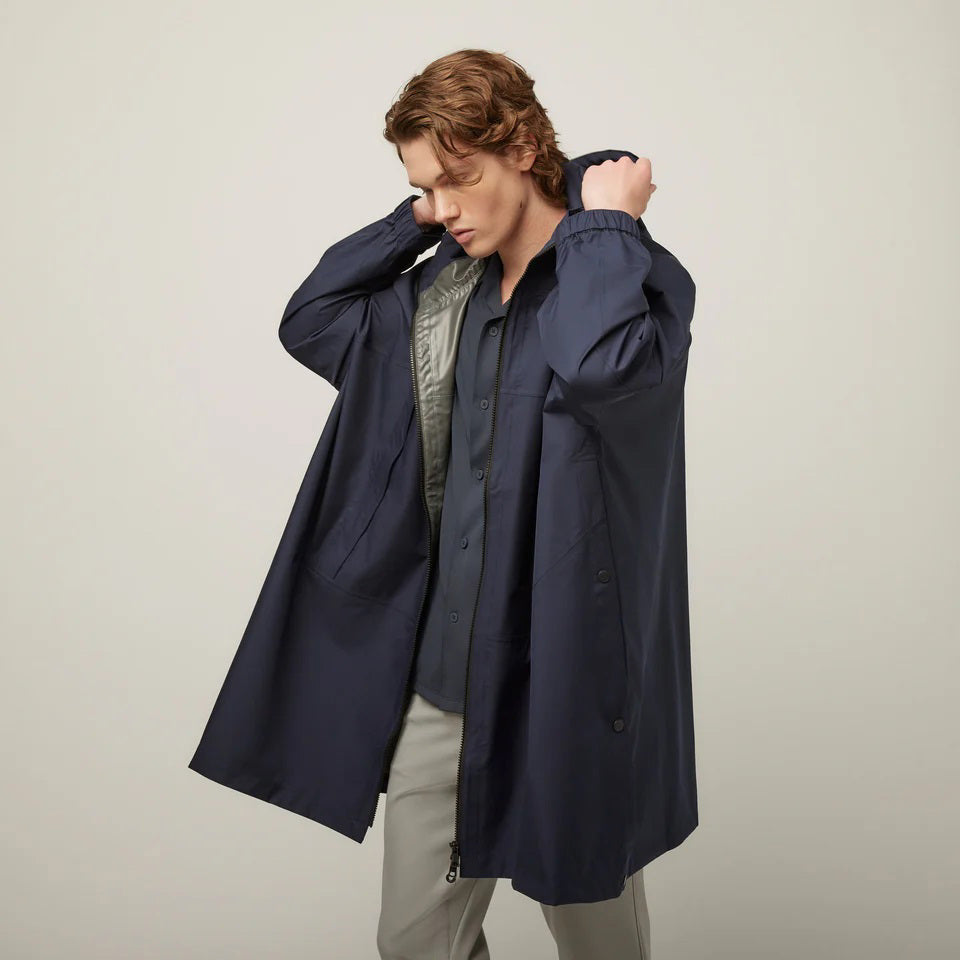 A person with short, wavy hair is seen from behind wearing the TILLEY - PACKABLE HOODED PONCHO by TILLEY in dark navy, featuring a hood and a loose, water-repellent fit, set against a plain light background.