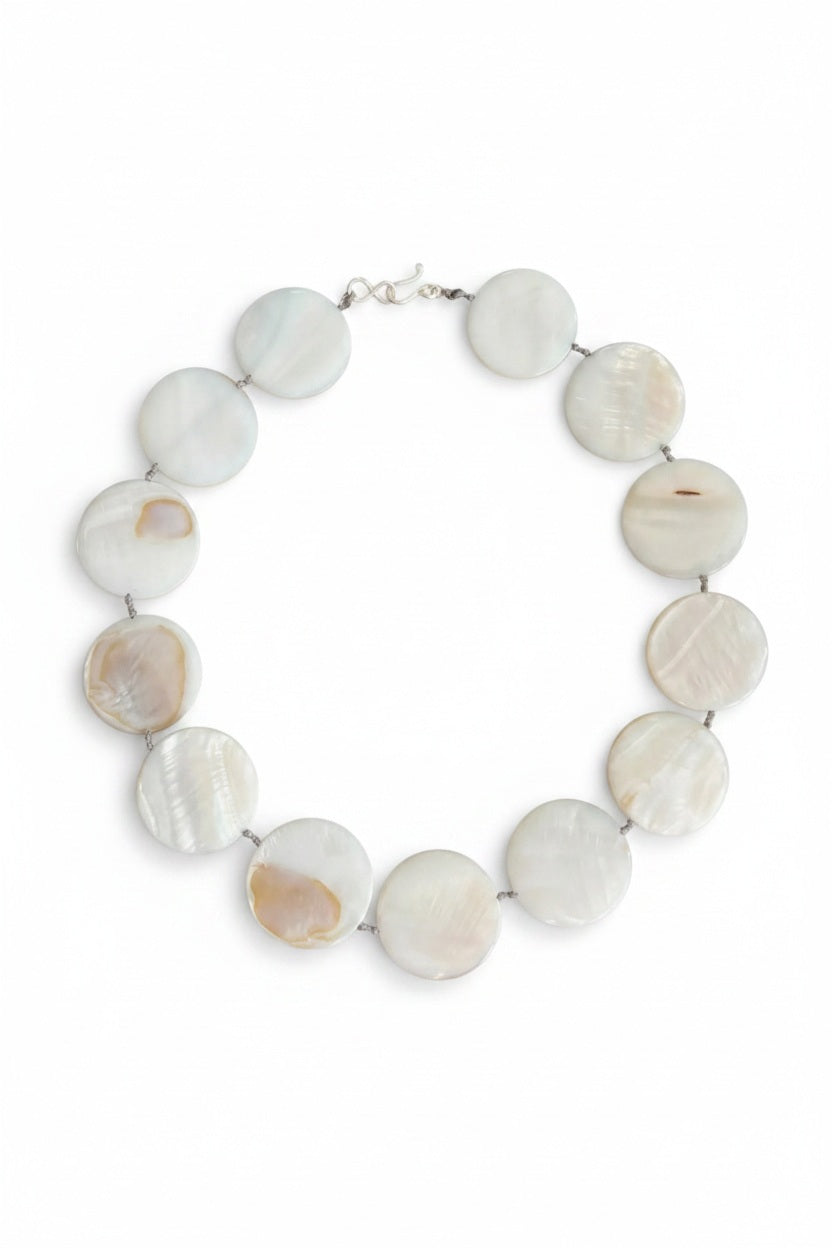 A mannequin is styled with a light gray shawl and showcases the ANN LIGHTFOOT Mother of Pearl Disc Ras du Cou Necklace, featuring large, round white beads and a sterling silver clasp, set against a neutral brown background.