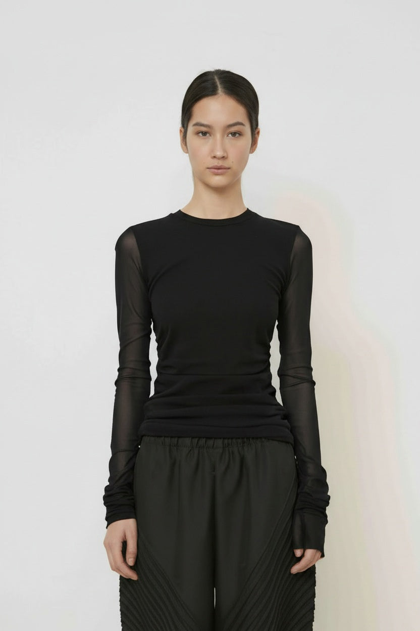 A woman with long dark hair in a low ponytail stands in profile against a plain light background, wearing the MEIMEIJ MESH LAYERING TOP by MEIMEIJ in red and a black skirt for a minimalist Italian fashion look.