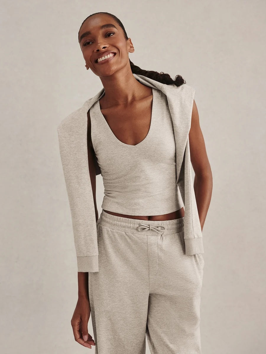 A woman wearing a light gray Varley Motion Easy Jogger 30 in Pebble Marl tank top and matching wide-leg joggers with athletic shoes.