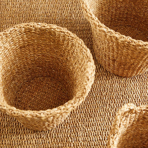The NAPA HOME AND GARDEN Seagrass Tapered Basket with Handles and Cuff, Large, is shown from above, highlighting its natural seagrass texture and expert craftsmanship on a matching surface.
