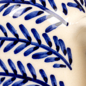 The HAND-PAINTED STONEWARE OIL CRUET WITH CORK STOPPER by CREATIVE COOP features blue leaf patterns and a handle, making it a perfect addition to rustic kitchen decor. Shown on a white background with the cork beside it.
