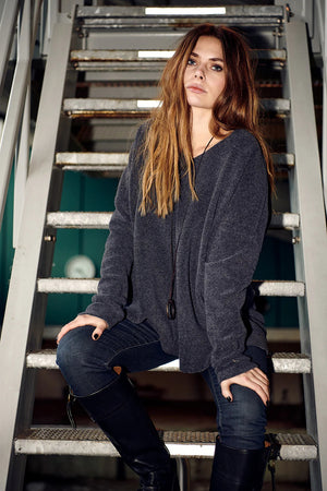 The HENRIETTE STEFFENSEN FLEECE V NECK SWEATER by HENRIETTE STEFFENSED is a loose-fitting, long-sleeve black sweater with a cozy V-neck, shown on a hanger and styled with a circular pendant necklace.