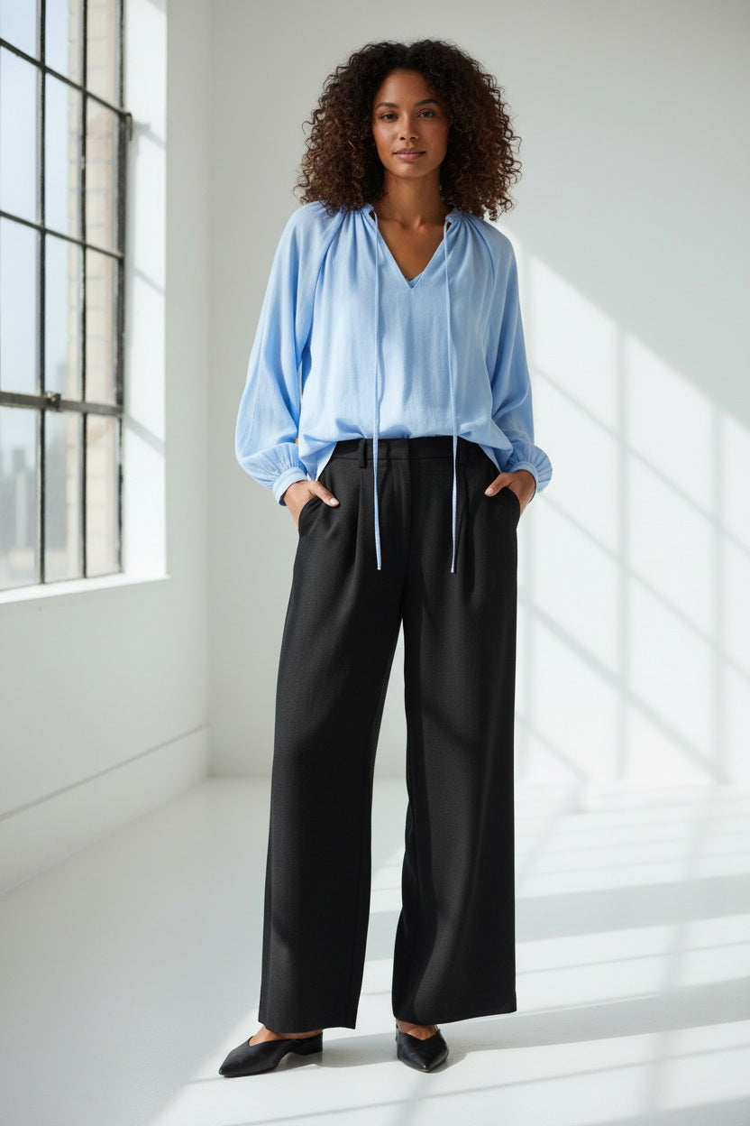 A person is shown from the shoulders down against a plain white background, wearing ELEH - BLACK PALAZZO TROUSERS by ELEH styled with black shoes and a loose-fitting, long-sleeve top.
