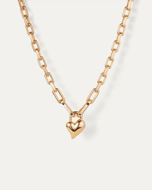 The JENNY BIRD HEART PENDANT NECKLACE showcases faceted gold chain links with a smooth, shiny heart charm at the center, elegantly set against a white background.