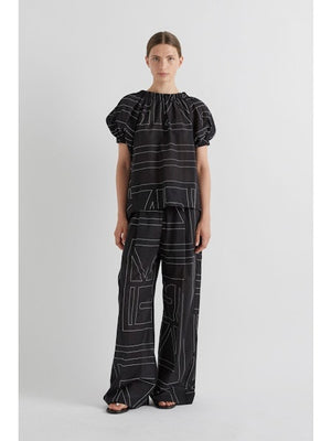 Model wears MEIMEIJ's ABSTRACT PRINT PANT—wide-leg black pants with a white abstract print—posing hands-in-pockets against a plain backdrop for a modern look.