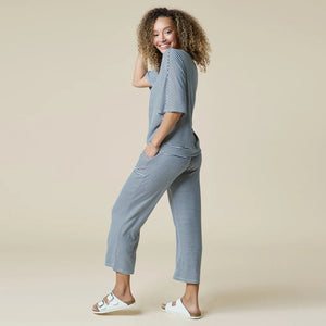 A woman wearing a light blue and white striped SOFTIES - DREAM RELAXED V-NECK WITH CAPRI LOUNGE SET with a V-neck, capri-length pants, and white sneakers.