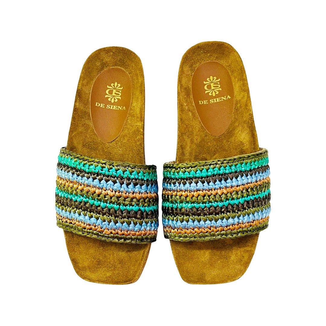 A pair of DA SIENA - LUCILLA RAFIA SLIDE sandals by DE SIENA features tan-colored soles with a raffia knotted top, adorned with multicolored stripes in shades of green, blue, brown, and yellow. The eco-style footbed is tan and showcases the brand's name and logo printed in gold, making it perfect for your summer style.