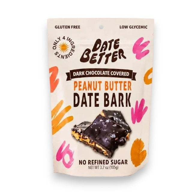 A bag of DATE BETTER - PEANUT DATE BARK by DATE BETTER SNACKS stands behind pieces of the bark arranged on a plate, with peanuts and a small bowl of salt nearby on a beige surface.
