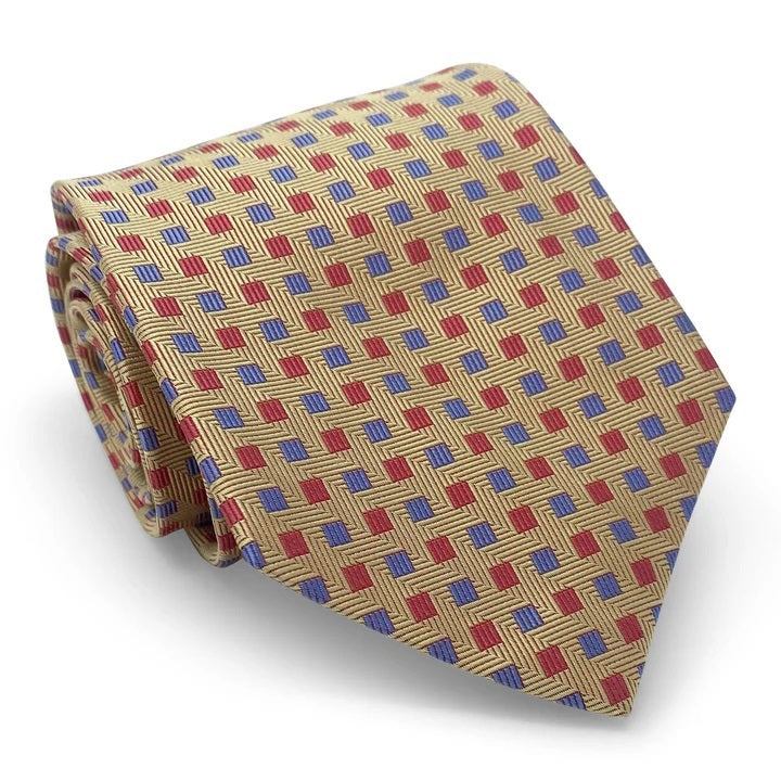 The BIRD DOG BAY PETER-BLAIR - BESPOKE SMALL SQUARES SILK TIE IN YELLOW is a rolled-up gold woven silk tie, showcasing a geometric pattern of red squares and small blue dots, with diagonal lines adding a textured appearance.