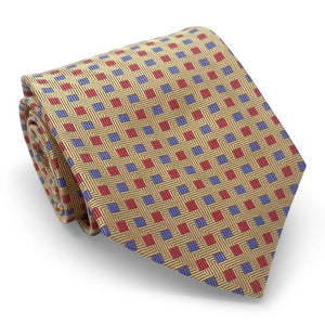 The BIRD DOG BAY PETER-BLAIR - BESPOKE SMALL SQUARES SILK TIE IN YELLOW is a rolled-up gold woven silk tie, showcasing a geometric pattern of red squares and small blue dots, with diagonal lines adding a textured appearance.