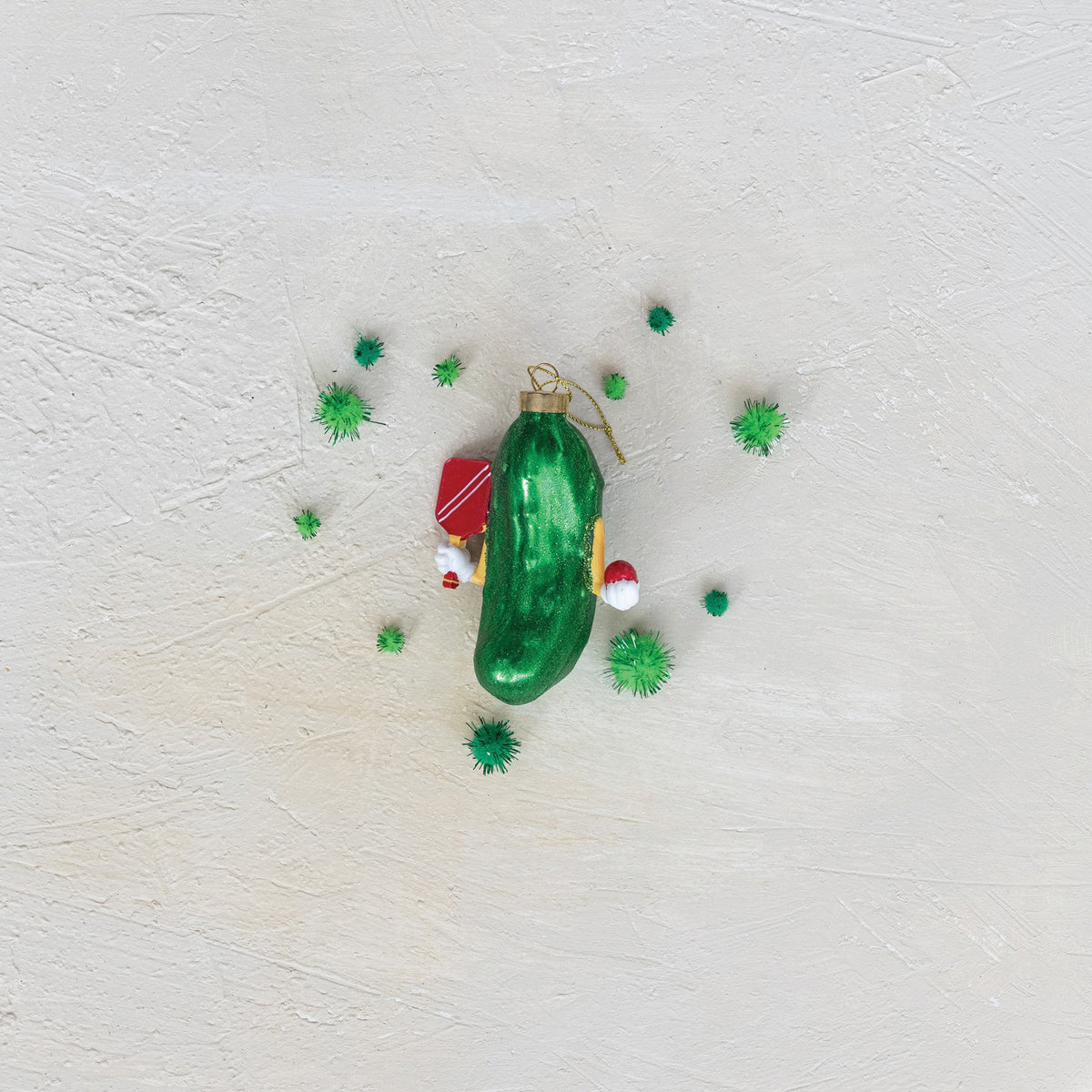 The CREATIVE COOP PICKLEBALL ORNAMENT is a green mercury glass pickleball-shaped Christmas decoration with a gold cap and hanging string, adorned with small red and white festive accents, shown on a white background.