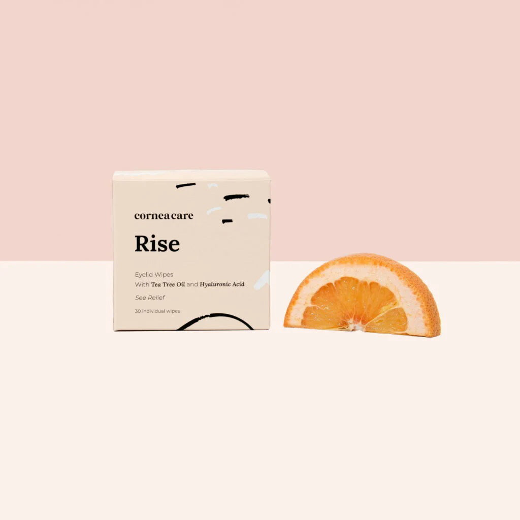 A CORNEA CARE packet, labeled &quot;CORNEACARE - RISE EYELID WIPES,&quot; sits against a light blue backdrop with abstract wave and dot patterns. Infused with tea tree oil, it elegantly alleviates eye dryness.