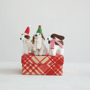 Three handcrafted FELT DOG ORNAMENT holiday decorations wearing festive hats and scarves perched atop a red plaid gift box.
