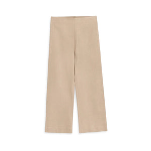 A woman with long hair stands indoors, hands on hips, wearing FRANK & EILEEN's WESTPORT ILLUSION WIDE LEG PULL-ON PANT in Champagne Glitter and white sneakers, facing away from the camera in a bright, spacious room.