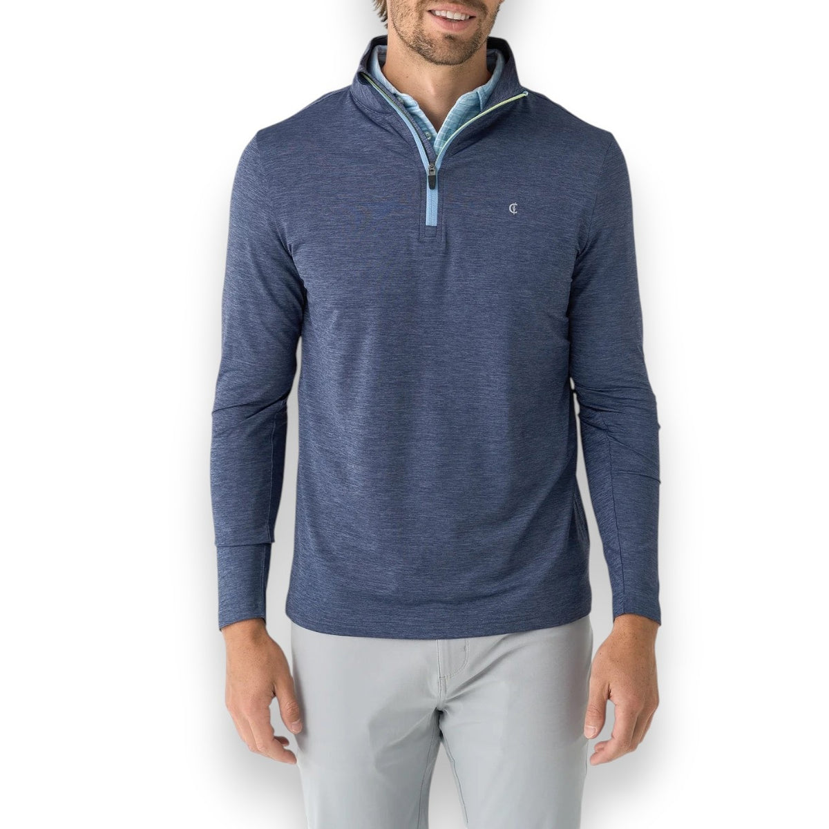 A person wears a CRIQUET - FEATHER PERFORMANCE KNIT QUARTER ZIP PULLOVER over a light blue checkered shirt. The moisture-wicking brrr° pullover by CRIQUET features a small embroidered logo on the left chest. Only the upper torso and neck are visible.