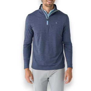 A person wears a CRIQUET - FEATHER PERFORMANCE KNIT QUARTER ZIP PULLOVER over a light blue checkered shirt. The moisture-wicking brrr° pullover by CRIQUET features a small embroidered logo on the left chest. Only the upper torso and neck are visible.