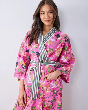 A person wearing a PRINTFRESH - BIRD & BLOSSOM LONG ROBE IN FUSCHIA, a long organic cotton robe with a bird and blossom pattern and green and white striped trim.