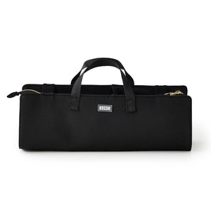 The KUSSHI - HAIR TOOLS TRAVEL BAG IN BLACK by KUSSHI is a rectangular neoprene organizer with two handles, gold zippers, and a white front label, shown against a white background.