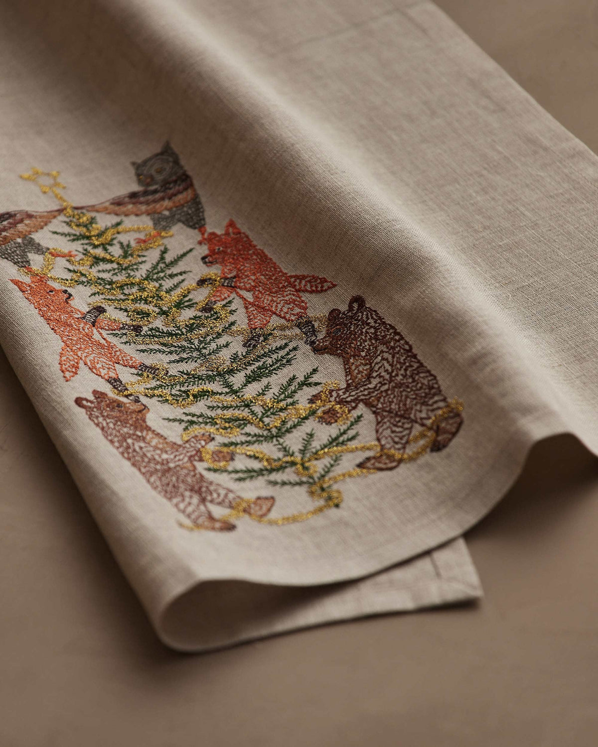 TINSEL TREE LINEN TEA TOWEL by CORAL & TUSK featuring embroidered owls, foxes, and bears decorating a tinsel tree for holiday decor.