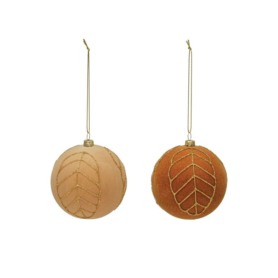 Nestled in a wooden box with straw-like filling on a light-colored surface are two VELVET BALL ORNAMENT 3&quot; by CREATIVE COOP, one in white and the other in copper, both adorned with glittering gold leaf patterns. These ornaments add an elegant touch to any holiday decor.