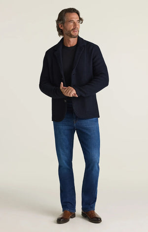 A person is shown from the back wearing a black shirt and the 34 HERITAGE - CASH BOOTCUT JEANS IN DARK BRUSHED VINTAGE by 34 HERITAGE. The vintage denim features back pockets and a black leather patch on the waistband, with the wearer’s arms visible.