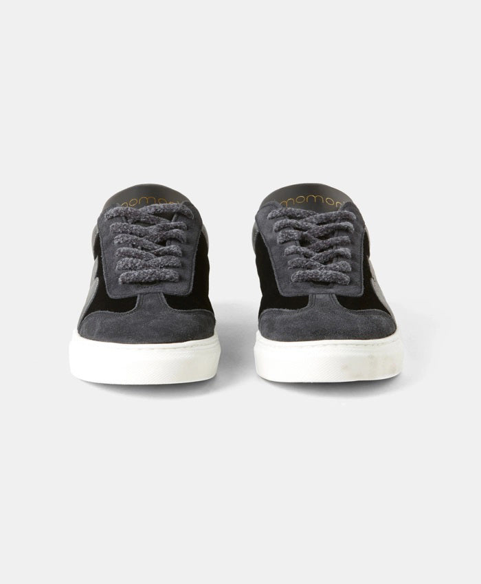 The iconic Momonì - Venezia Sneakers by MOMONI, showcasing black leather uppers and gray laces, are positioned side by side, facing forward. They feature white box soles and a logo on the tongue area. The background is a plain white surface.