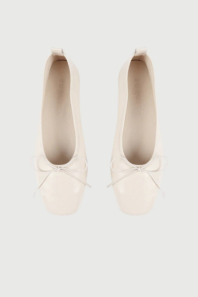 The Augusta - Sienna Ballet Flat by AUGUSTA is a single silver-colored shoe featuring a subtle metallic sheen and a simple bow on the front. It has a low brown sole and a pull tab at the back. Handcrafted in Spain from leather, this ballet flat is shown from the side against a light gray background.