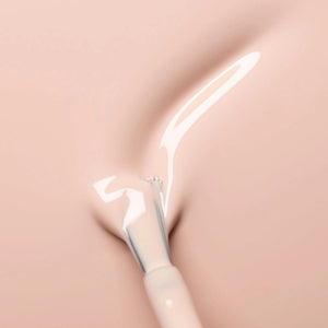 A hand with neatly manicured nails—polished with MANUCURIST - GREEN™ Nail Polish in Pastel Pink by MANUCURIST INC—rests on light brown sand, a few grains clinging to the skin.