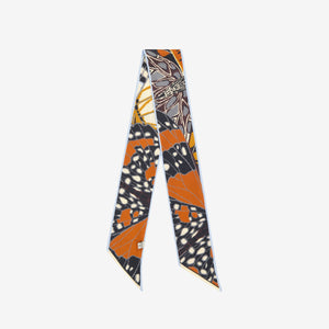 A woman wears a dark denim top paired with the INOUI EDITIONS - PAPILLON (BUTTERFLIES) silk ribbon by INOUI, styled as a chic neck accessory featuring butterfly and animal print patterns.