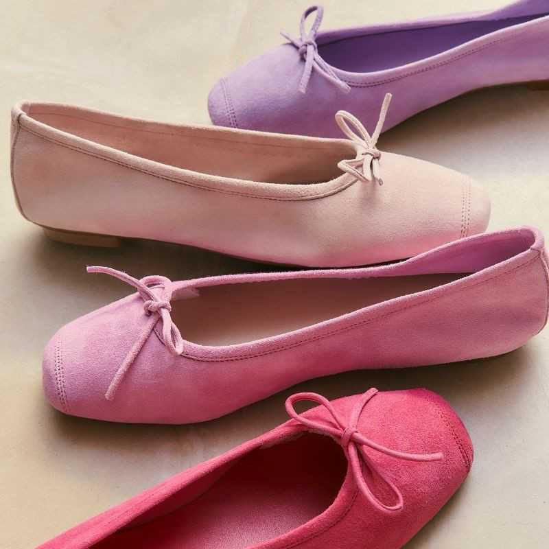 A close-up of the REQINS - HARMONY SUEDE BALLERINA FLATS IN PINK, featuring a bow detail on the front, photographed on a light surface—an elegant update to this classic women’s shoe by REQINS.