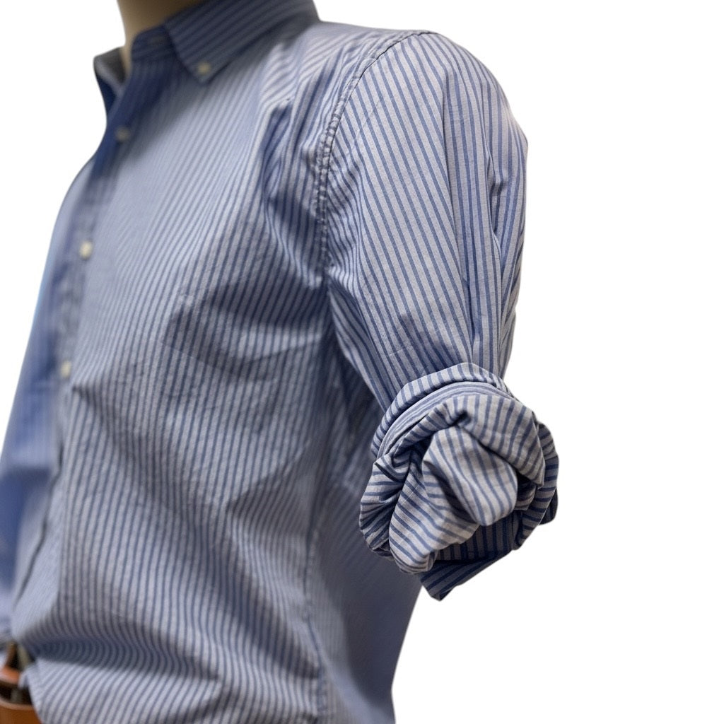 A man in a FRANK &amp; EILEEN Finbar Men's Button Up Shirt in Blue Stripes, blue jeans, and white sneakers walks confidently down a sunny, tree-lined cobblestone street.