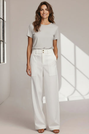Wearing HINSON WU’s KELLY TRAVELERS TWILL PANT IN WHITE—high-waisted, wide-leg with large front pockets, front seam, and double button closure—paired with black pointed-toe shoes. Torso partially visible against a plain background.