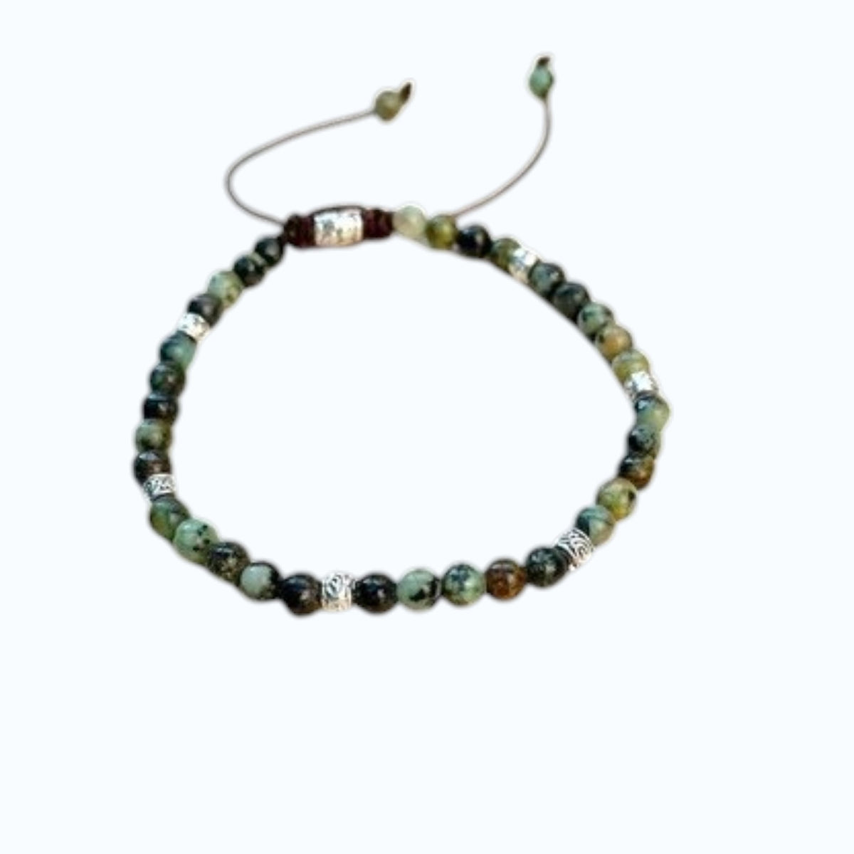 The STOLEN RICHES Formentera Bracelet in African Turquoise Stone features green and brown beads with silver accents on an adjustable brown cord, adding earthy elegance to any style.